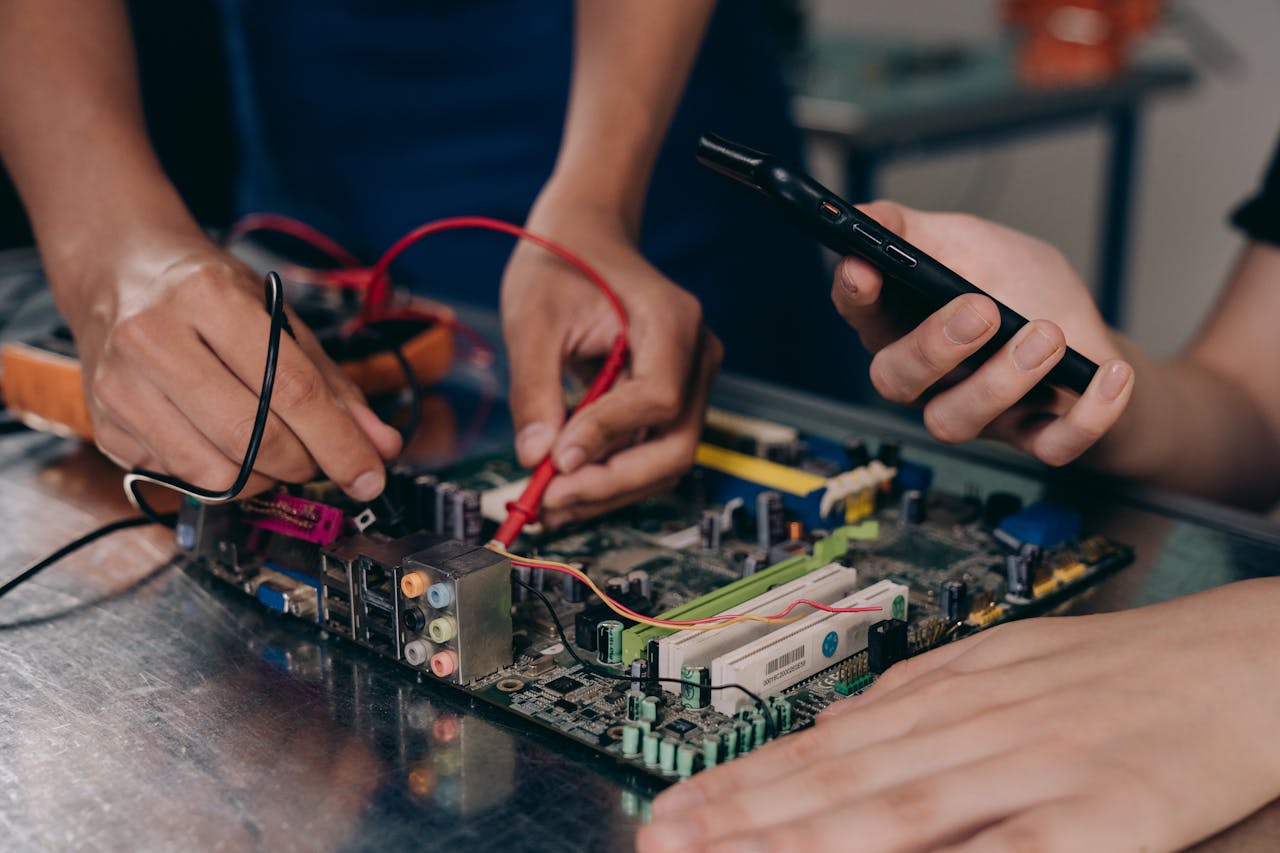 who-we-are-img Close-up of hands working on a motherboard using electrical tools and tester.